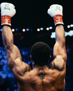 Anthony Joshua raising both white Everlast boxing gloves high in victory to salute the crowd following his comeback win against Kristian Prenga.