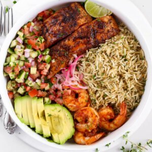 Kikifoodies garlic herb rice served in a bowl with pan-seared salmon, grilled shrimp, sliced avocado, pickled onions, and cucumber tomato salad.