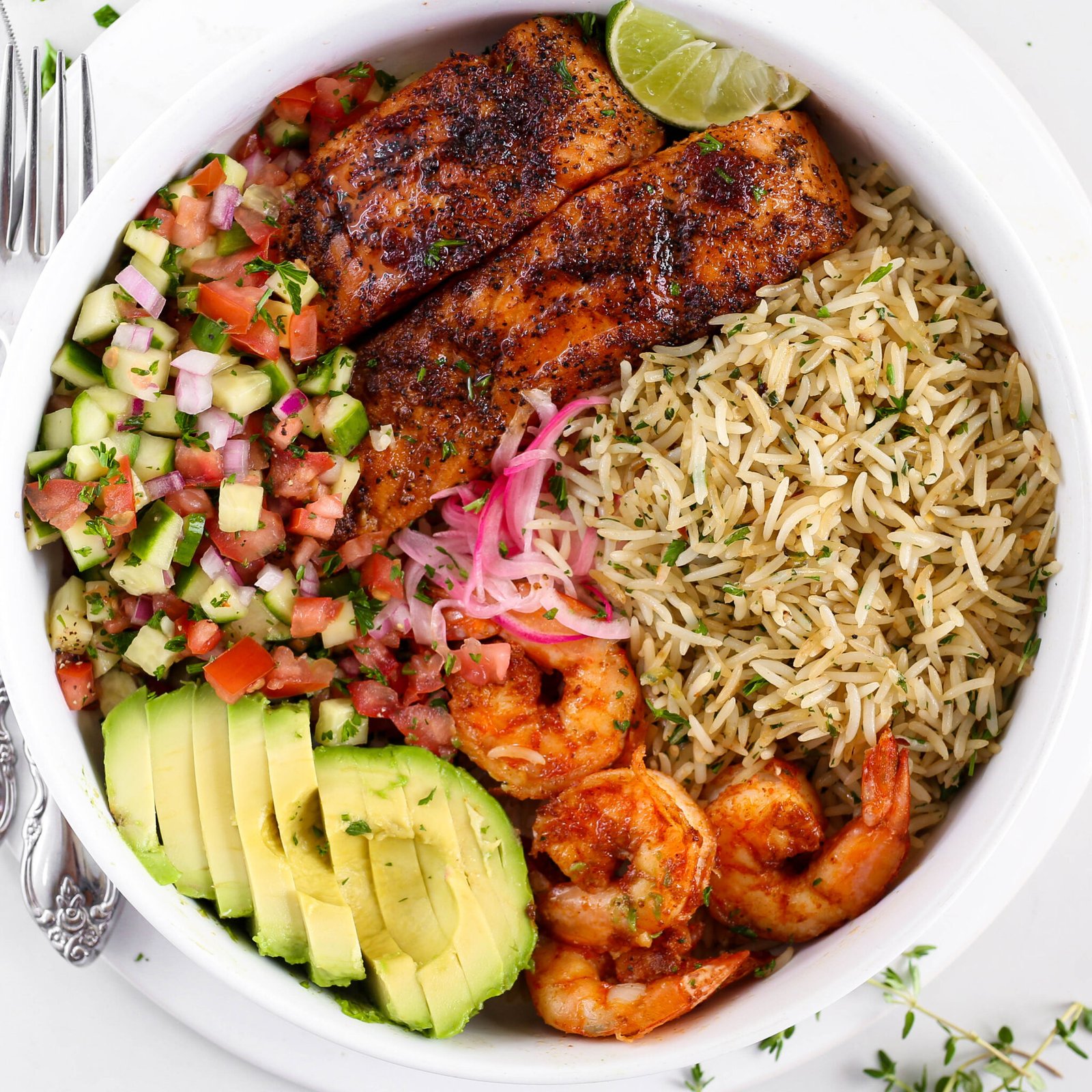 Kikifoodies garlic herb rice served in a bowl with pan-seared salmon, grilled shrimp, sliced avocado, pickled onions, and cucumber tomato salad.