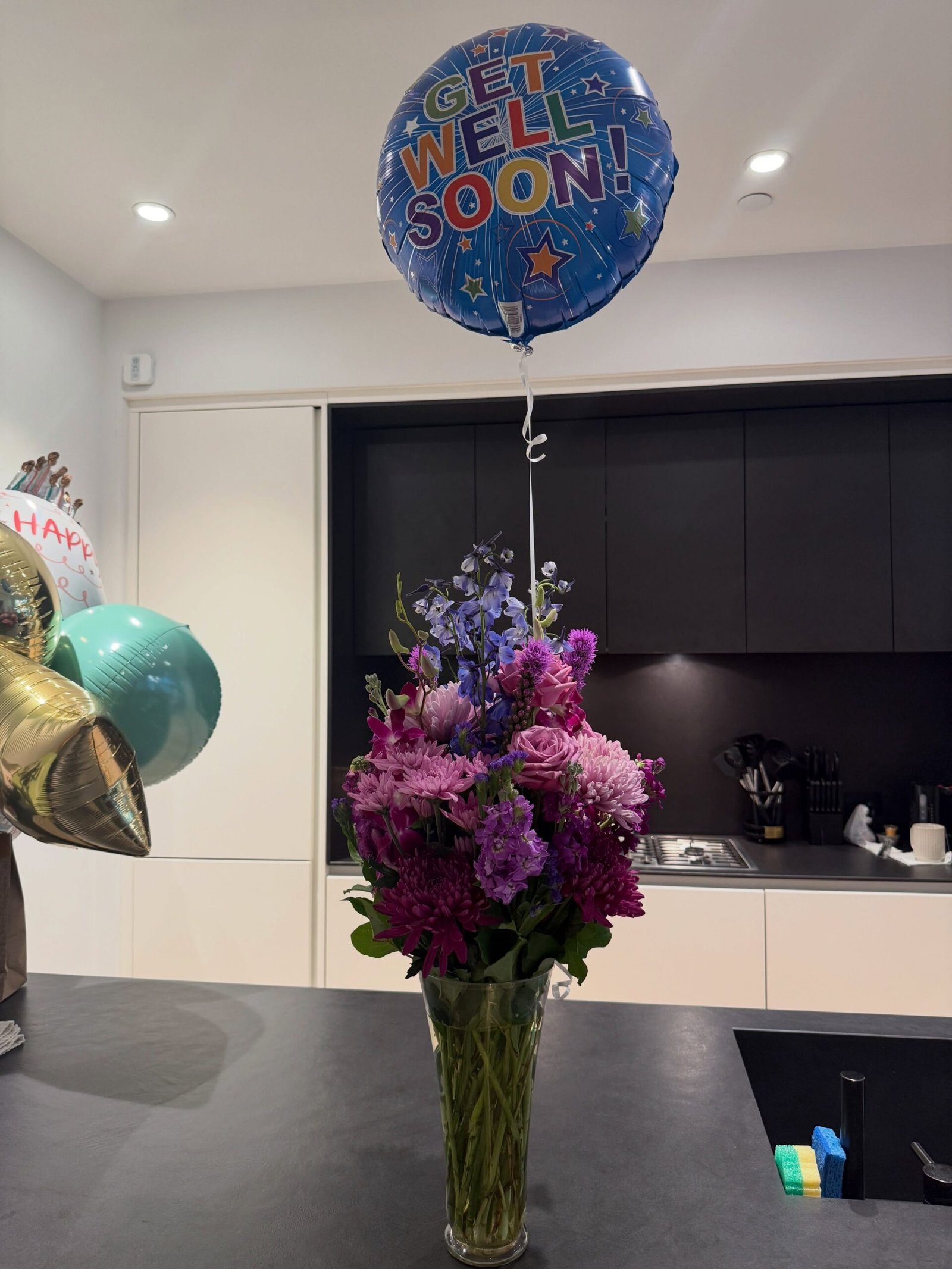 Purple and pink floral arrangement with a Get Well Soon balloon sent to Ayra Starr following major surgery recovery.