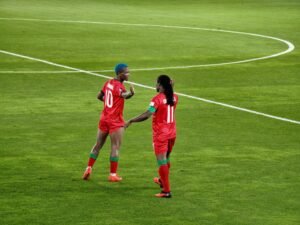 Temwa Chawinga in blue hair wearing jersey number 10 reaching out to sister Tabitha Chawinga wearing jersey number 11 on the pitch.