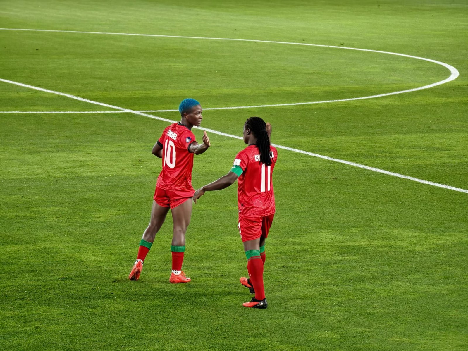 Temwa Chawinga in blue hair wearing jersey number 10 reaching out to sister Tabitha Chawinga wearing jersey number 11 on the pitch.