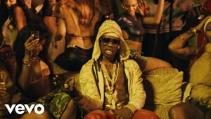Mavin Records artist Rema wearing a pattern-patterned hooded jacket, sunglasses, and layered gold butterfly necklaces in a scene from his official TEA music video.