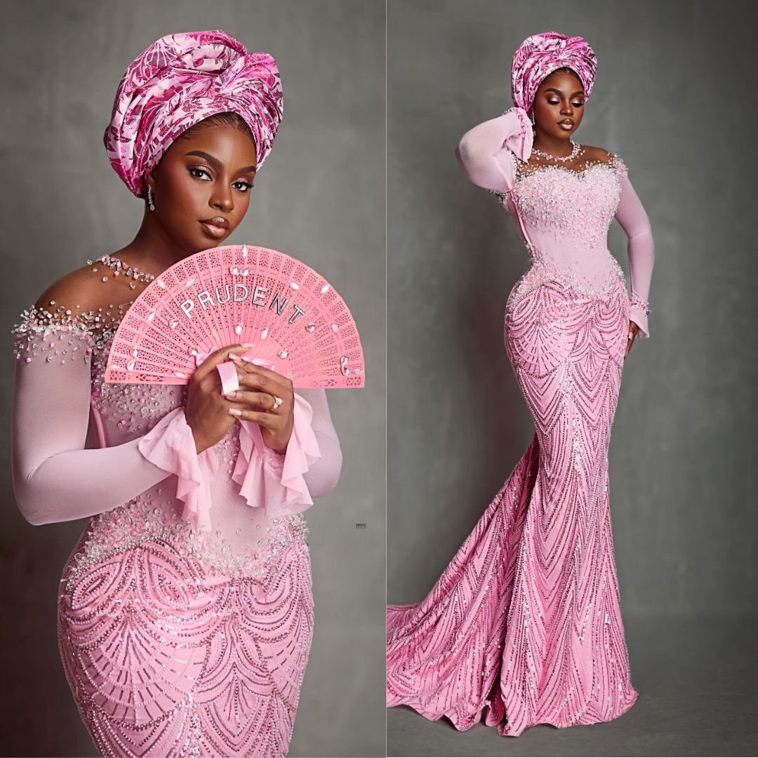Prudent Gabriel wearing a pink mermaid gown with sheer long sleeves, shoulder beadwork, and a structured Gele at Akin Faminu traditional wedding.