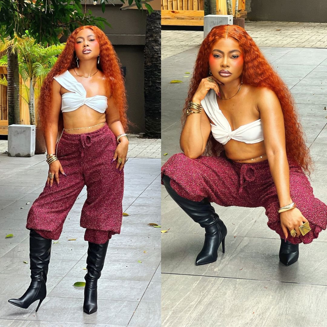 Teniola Aladese wearing a white twisted crop top, deep magenta trousers, and black knee-high leather boots