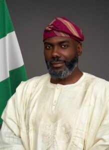 Olugbile Holloway, Director-General of the National Commission for Museums and Monuments (NCMM), wearing traditional white Agbada and a magenta striped Fila cap beside the Nigerian flag