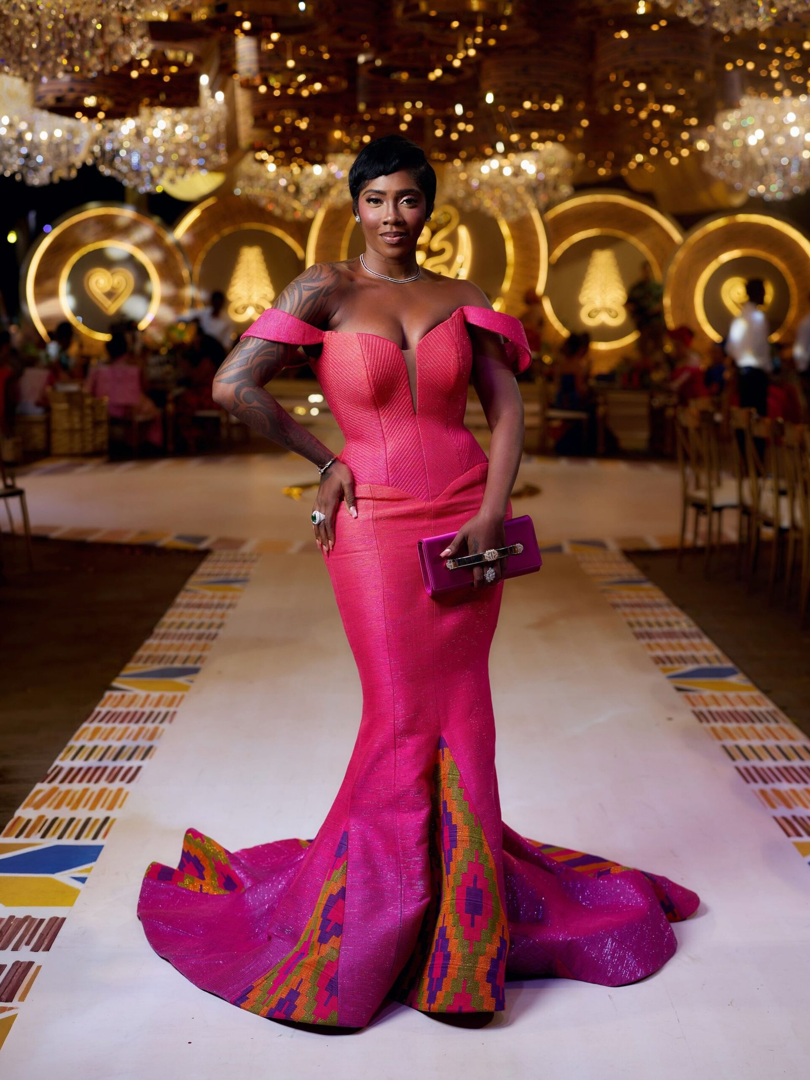 Nigerian singer Tiwa Savage posing in a vibrant hot pink off-shoulder gown with patterned Kente hemline at Bozoma Saint John’s traditional Ghanaian wedding in Accra.