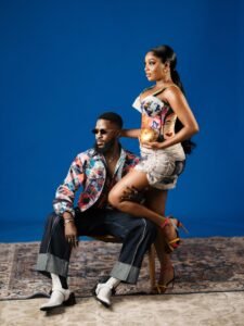 Akin Faminu seated in dark trousers and a graphic shirt with Kiky Festus posing in a Vogue magazine print mini dress.