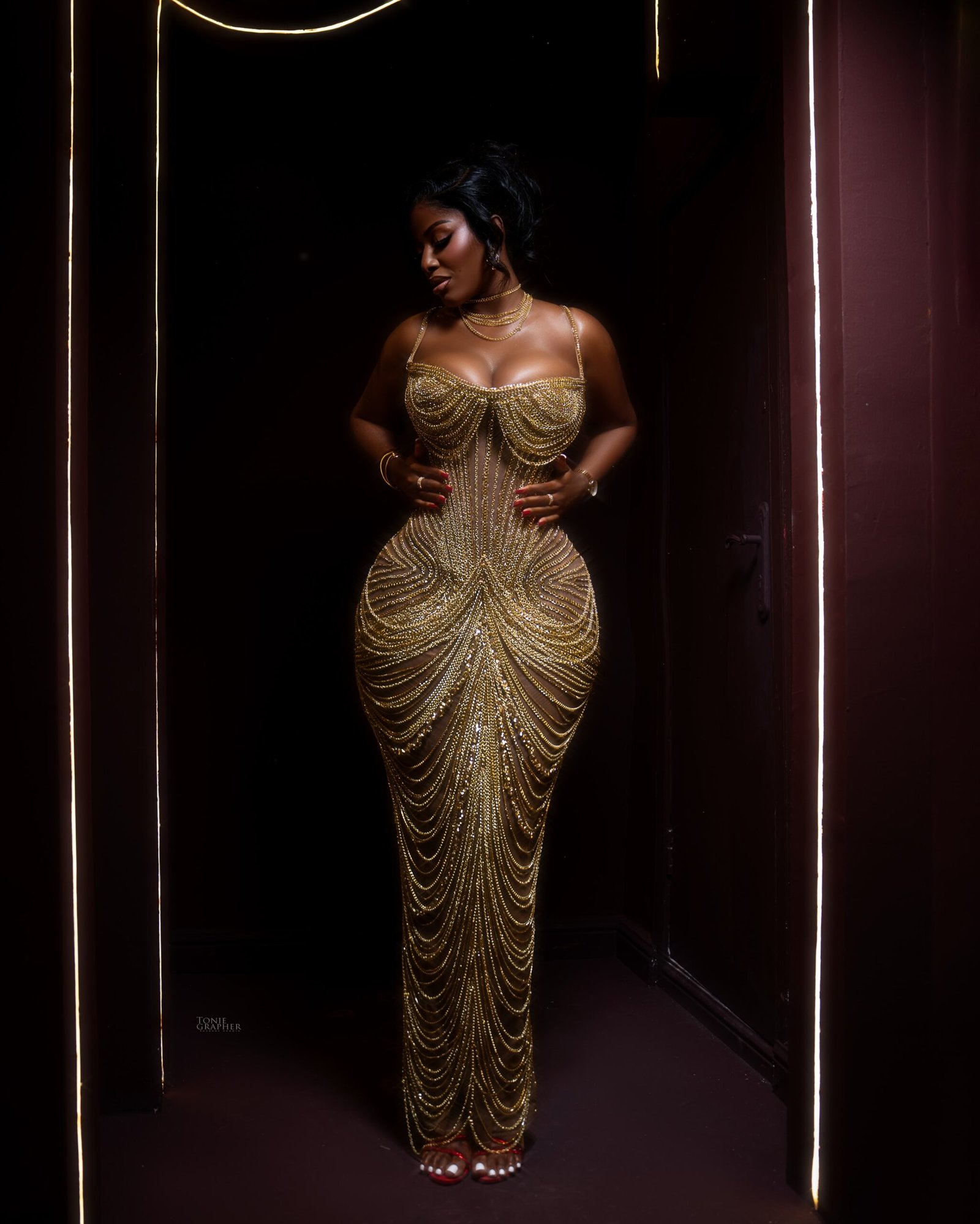 Hilda Baci posing with hands on her waist wearing a floor-length gold metallic chainmail gown.
