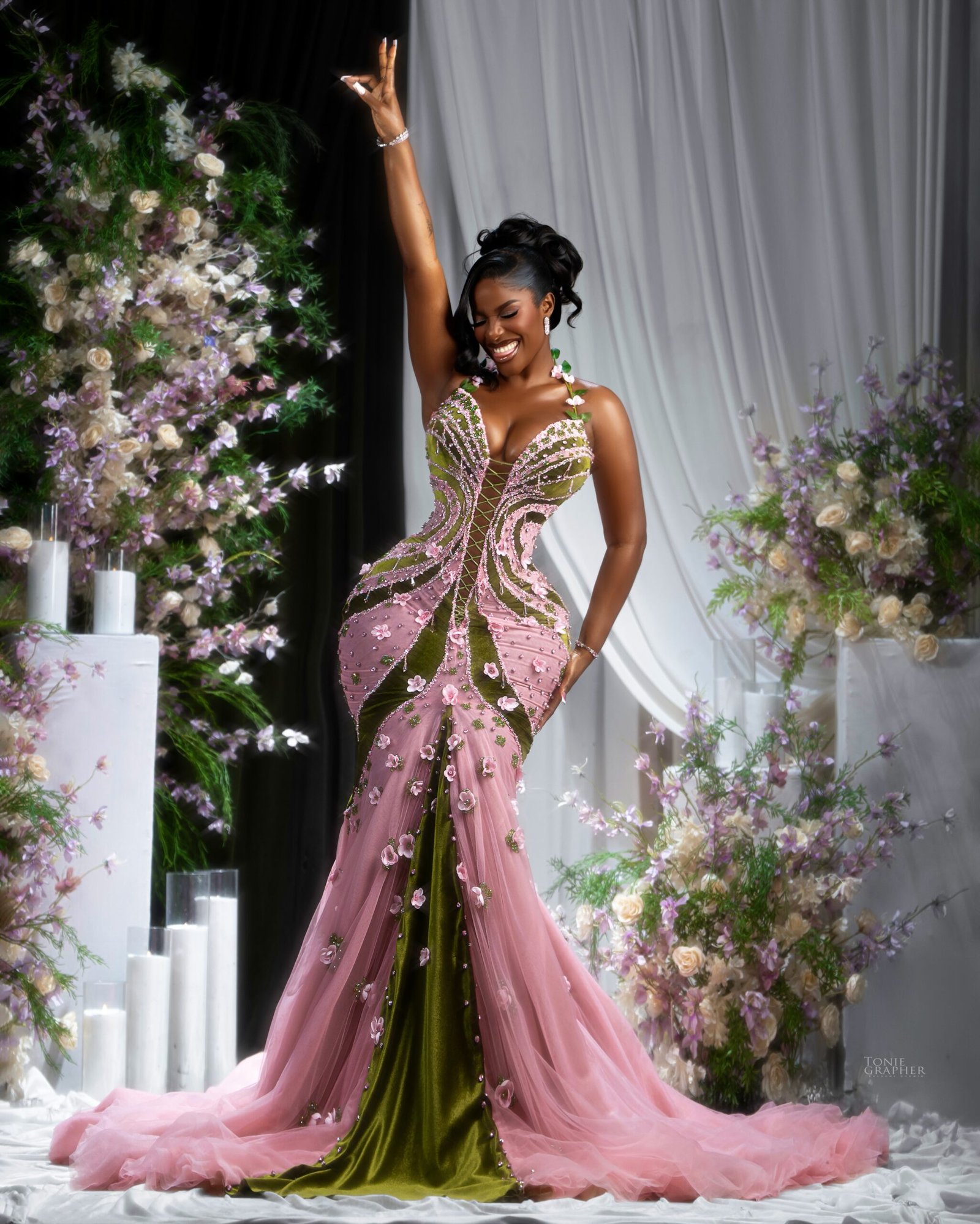 Hilda Baci raising one arm in celebration while wearing a pink and olive green corseted floral gown.