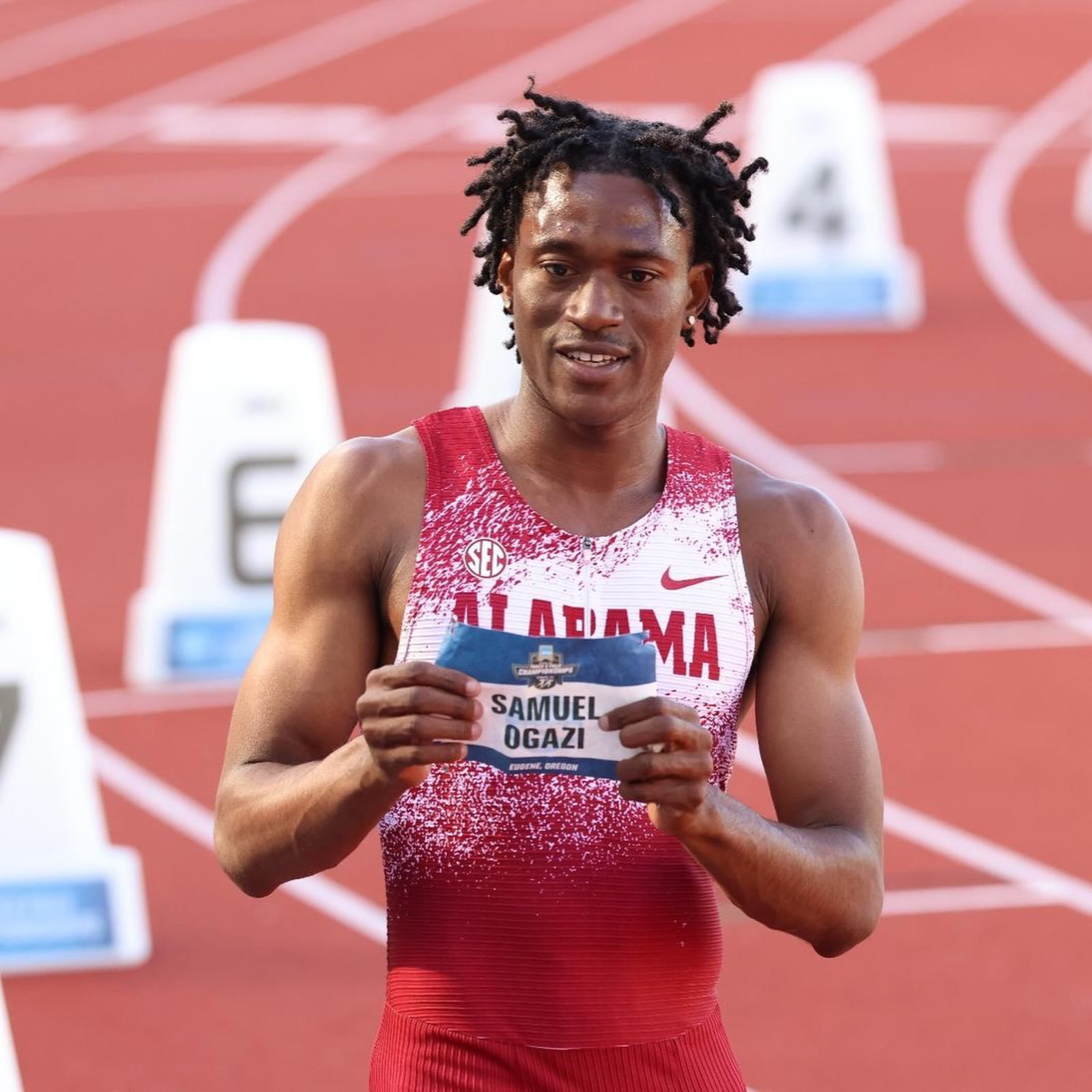 Samuel Ogazi holding his race bib in an Alabama Track and Field kit on the running track.