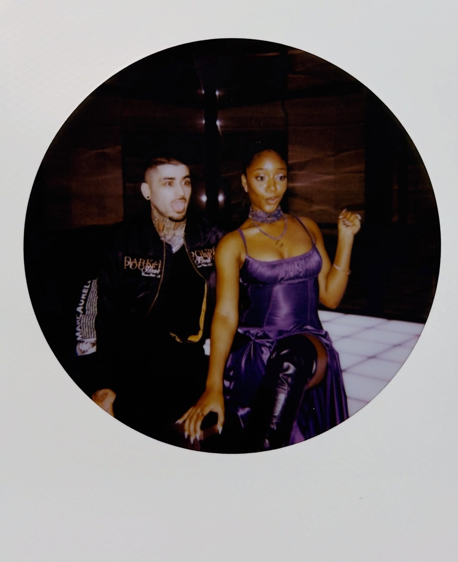 Zayn Malik sticking his tongue out next to Ayra Starr gesturing on a lit-up floor in a circular polaroid frame.