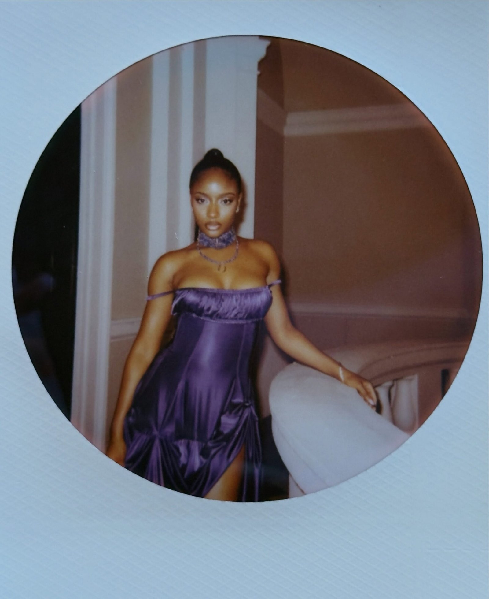 Ayra Starr posing in a purple satin slit dress with a matching beaded choker and thigh-high boots in a circular polaroid frame.