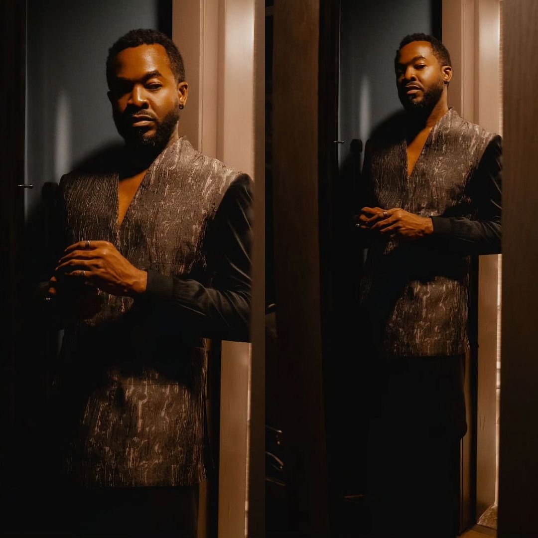 OC Ukeje wearing a dark textured longline tunic vest over a long sleeve shirt for the BellaNaija 20th anniversary celebration.