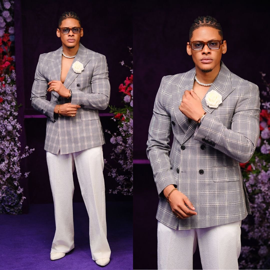Elozonam wearing a grey plaid double-breasted suit jacket with a white lapel flower and white wide trousers at BellaNaija event.
