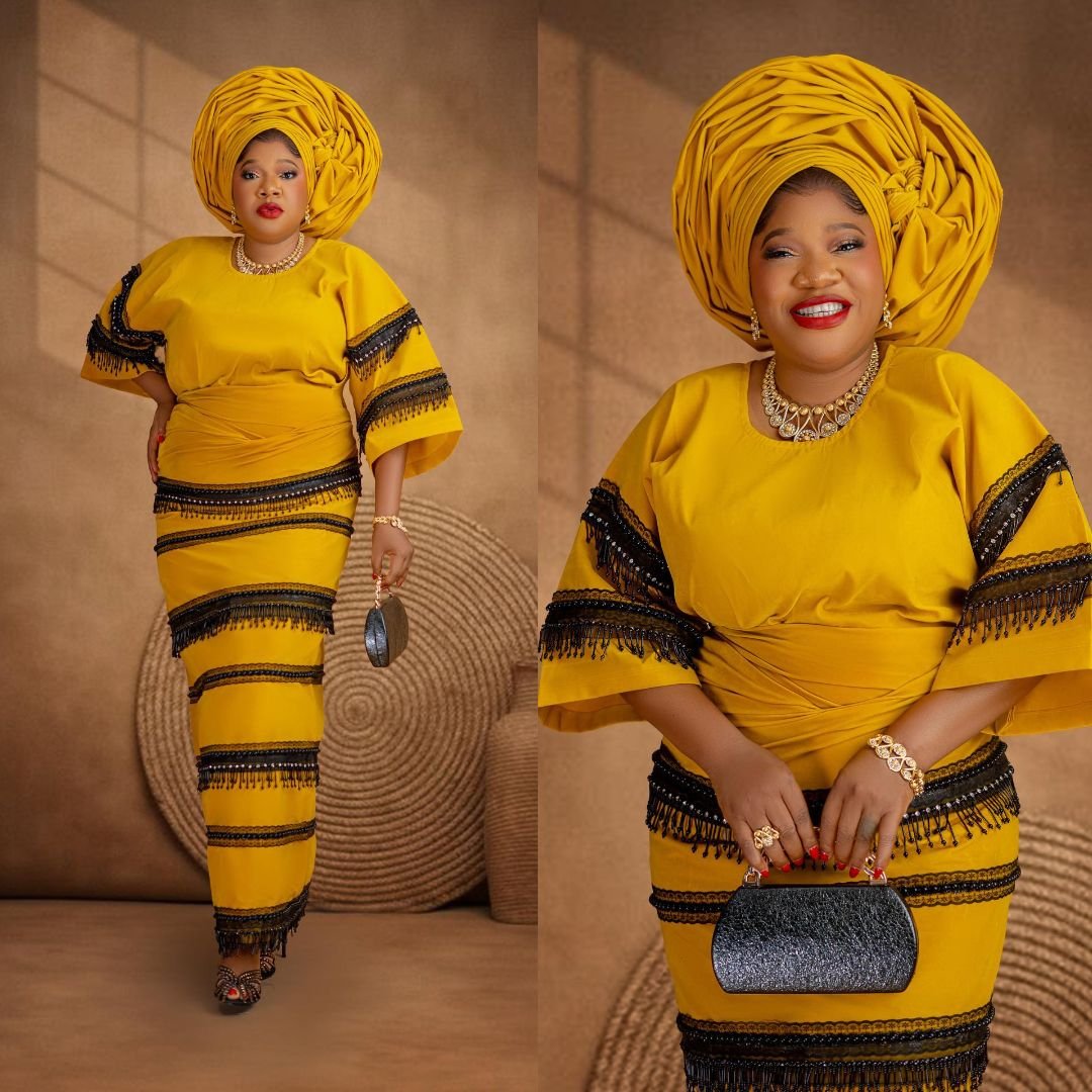 Toyin Abraham Ajeyemi wearing a mustard yellow buba and iro with horizontal black lace bands and fringe details.