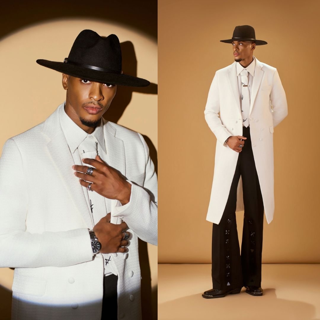 Henry Orakwue wearing a white floor-length coat, black wide trousers, and a black fedora hat at BellaNaija red carpet.
