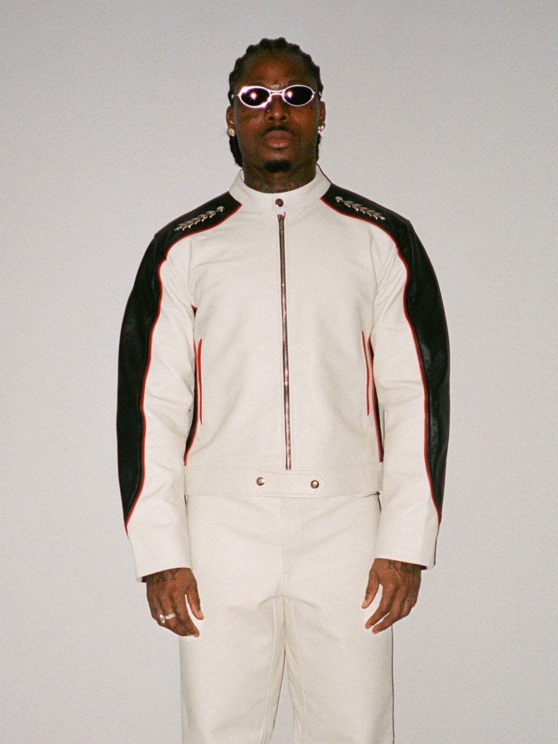 Asake wearing a white and black leather biker suit with oval sunglasses reflecting his Mr Money persona.