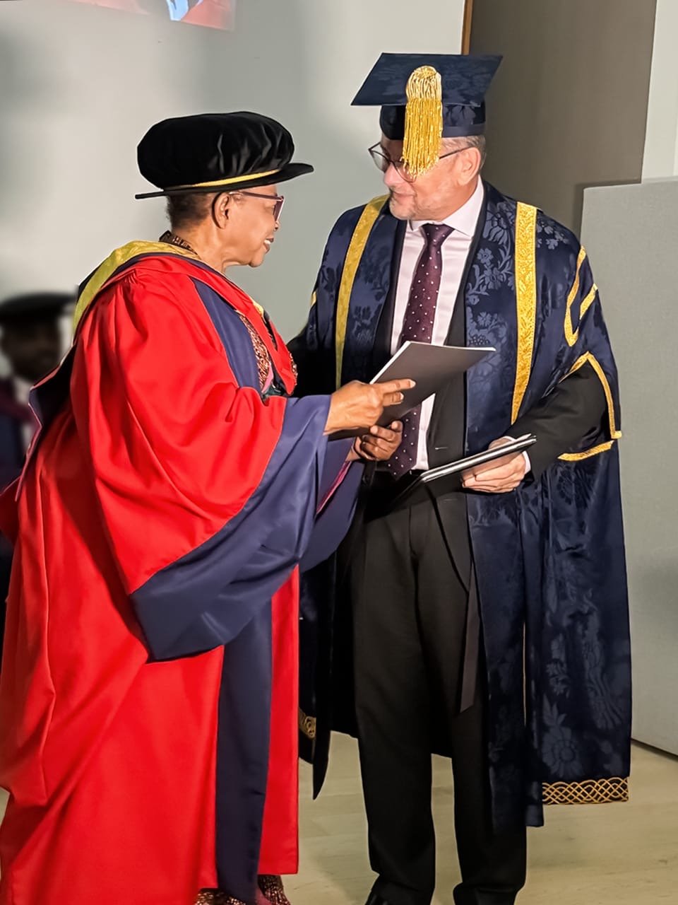 Folorunso Alakija in a red doctoral gown receiving her honorary degree certificate from Vice-Chancellor Professor David Cole.